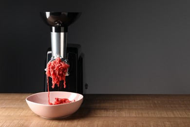 Photo of Electric meat grinder with beef mince on wooden table against grey background. Space for text