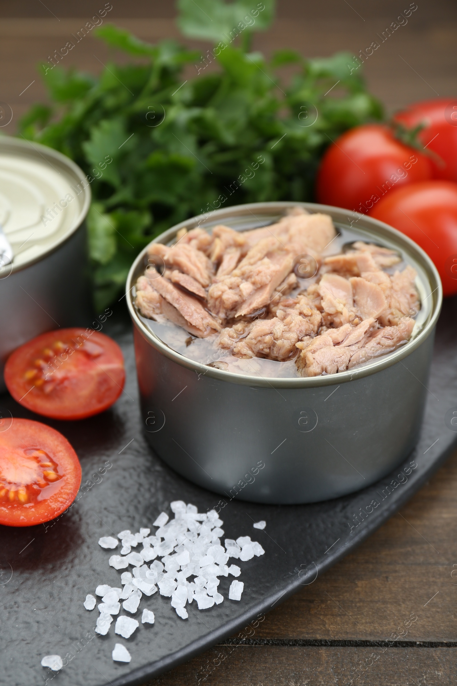 Photo of Tin can with canned tuna, salt and tomatoes on wooden table, closeup