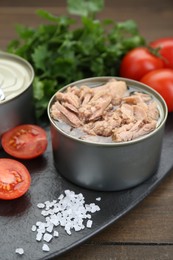 Tin can with canned tuna, salt and tomatoes on wooden table, closeup