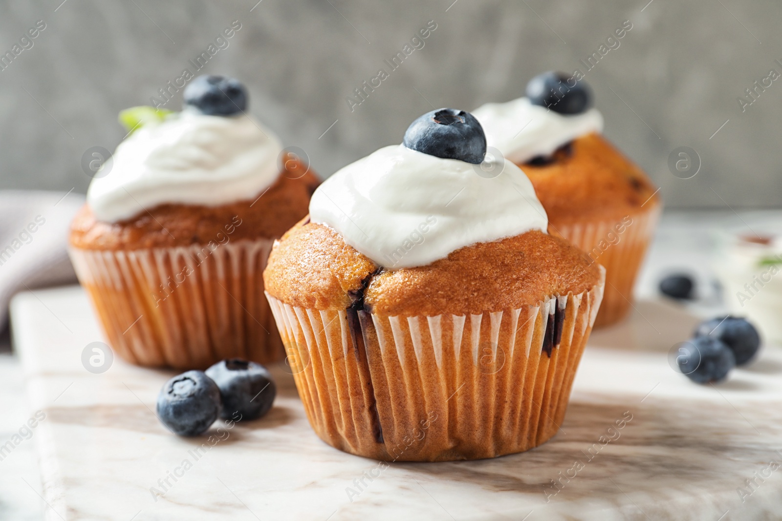 Photo of Marble board with tasty muffins, cream and blueberries on table