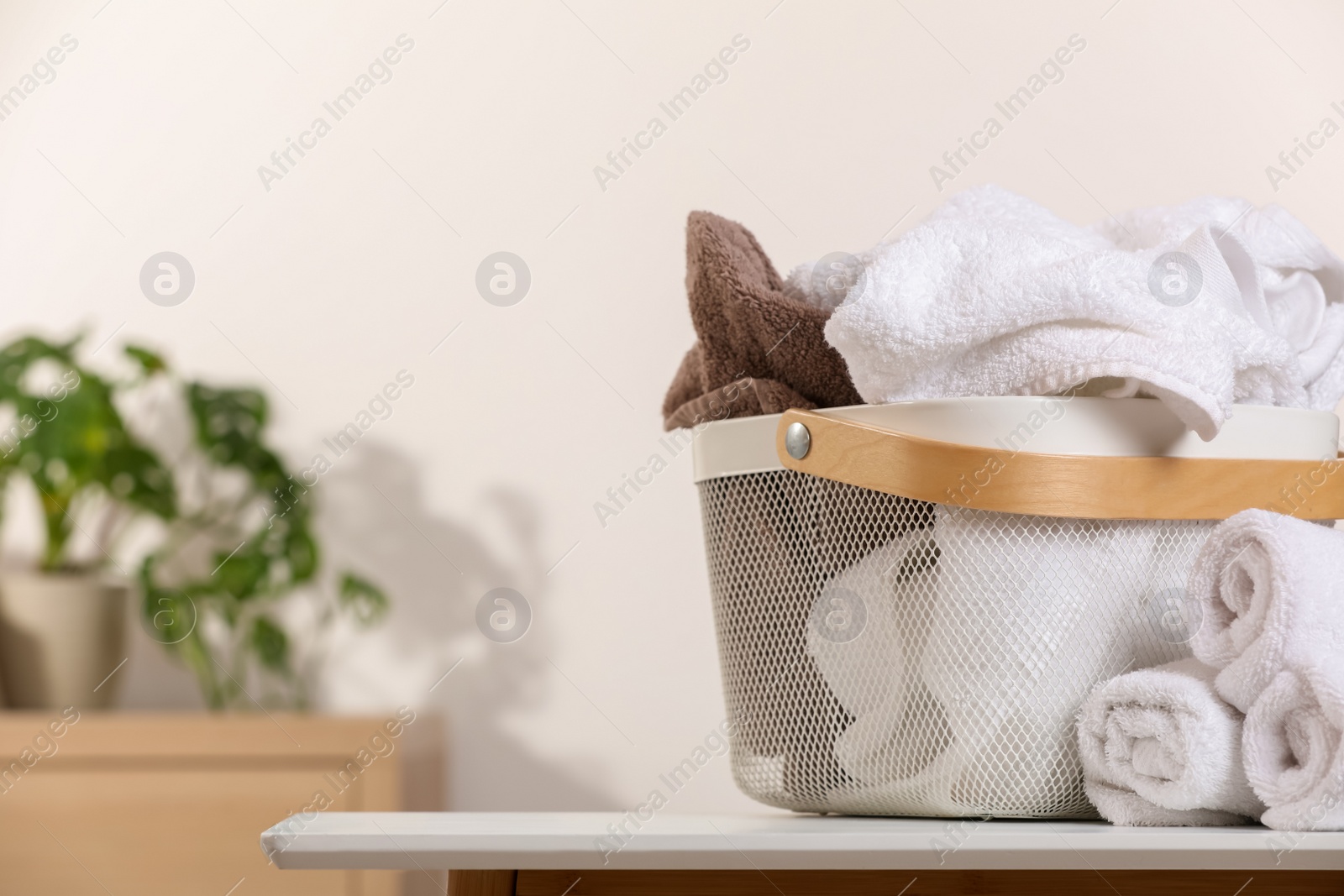 Photo of Laundry basket overfilled with clothes near rolled towels on white table indoors. Space for text