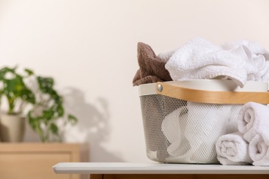 Laundry basket overfilled with clothes near rolled towels on white table indoors. Space for text