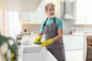 Photo of Senior man in protective gloves washing plate above sink in kitchen