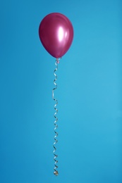 Bright balloon with ribbon on color background