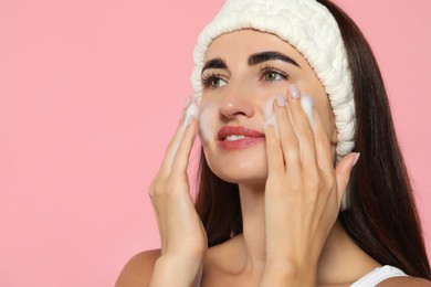 Photo of Beautiful woman applying cleansing foam onto face on pink background. Space for text