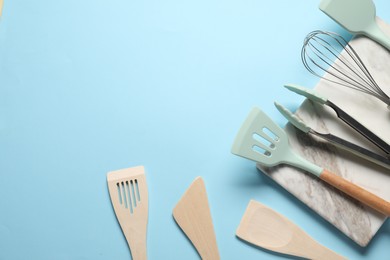 Photo of Different spatulas, whisk and tongs on light blue background, flat lay. Space for text