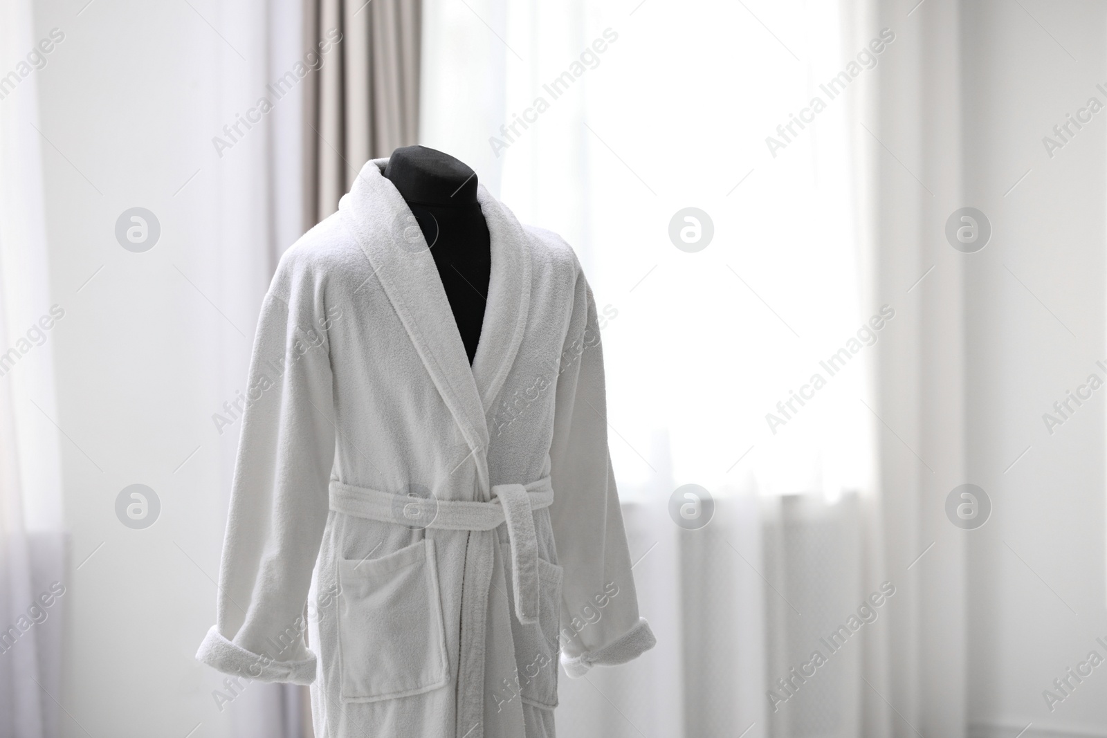 Photo of Soft comfortable bathrobe on mannequin in room, space for text