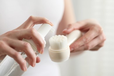 Washing face. Woman applying cleansing foam onto brush against light background, closeup