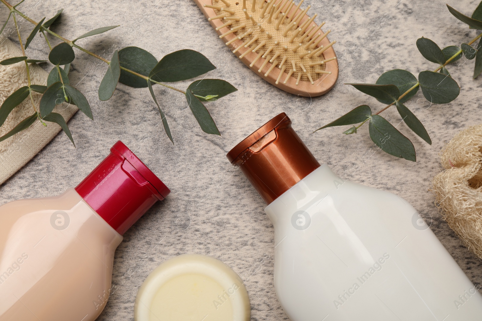 Photo of Shampoo bottles, solid shampoo bar, hair brush and green leaves on grey textured table, flat lay