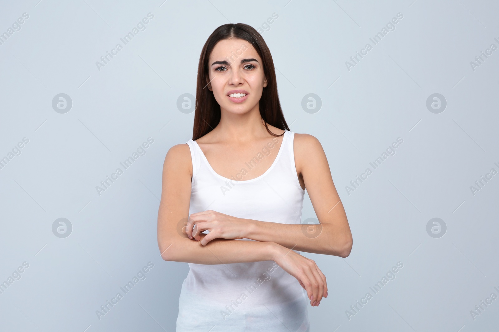 Photo of Young woman scratching arm on light background. Annoying itch