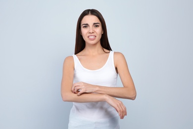 Young woman scratching arm on light background. Annoying itch