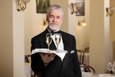 Photo of Senior butler holding tray with glasses of sparkling wine in restaurant
