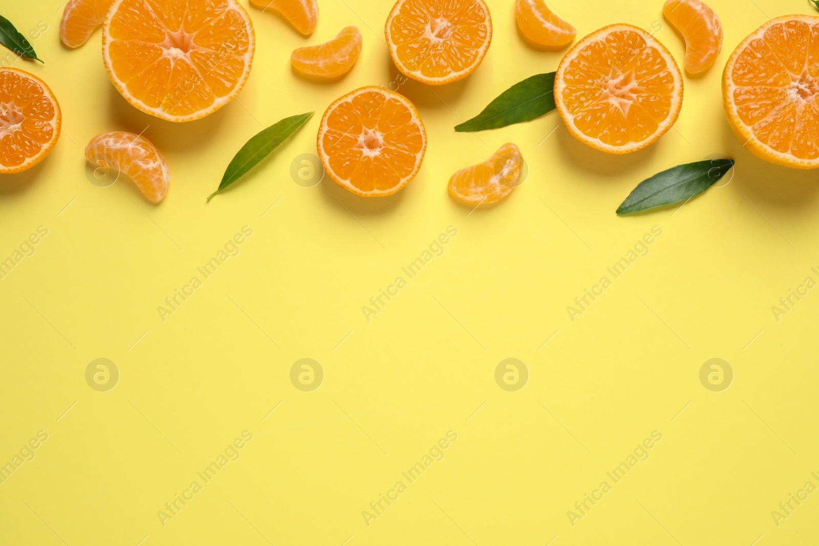 Photo of Flat lay composition with fresh ripe tangerines and leaves on light yellow background, space for text. Citrus fruit