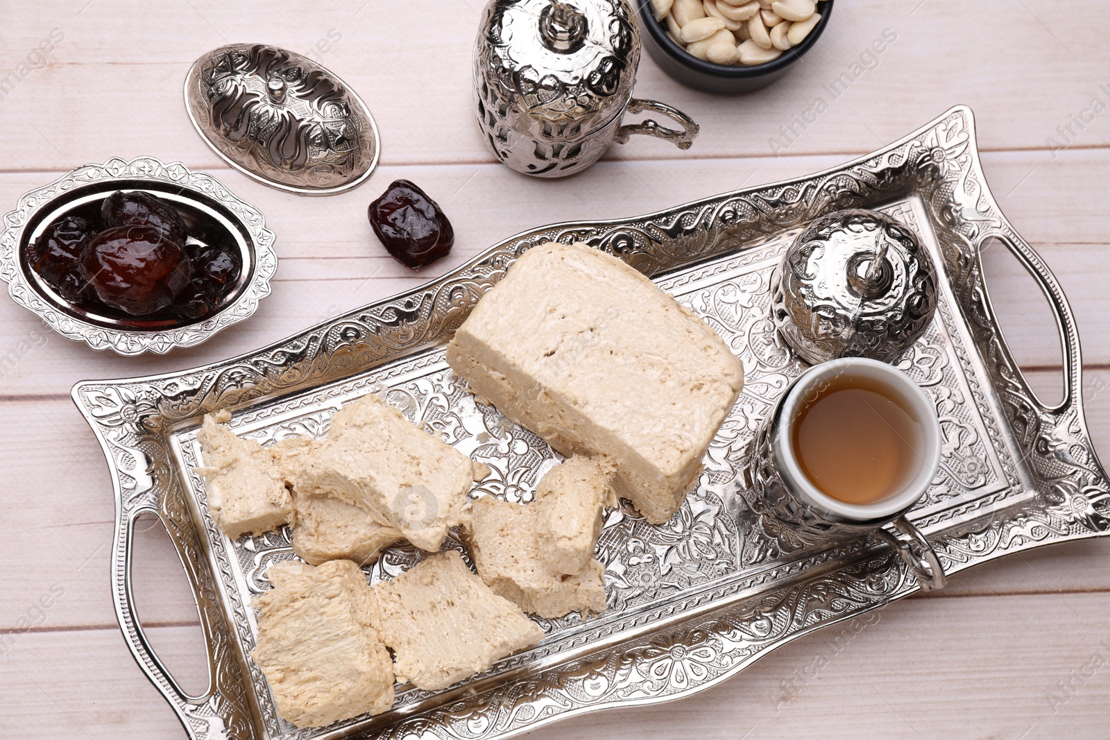 Photo of Pieces of tasty halva, tea and dates on light wooden table, above view