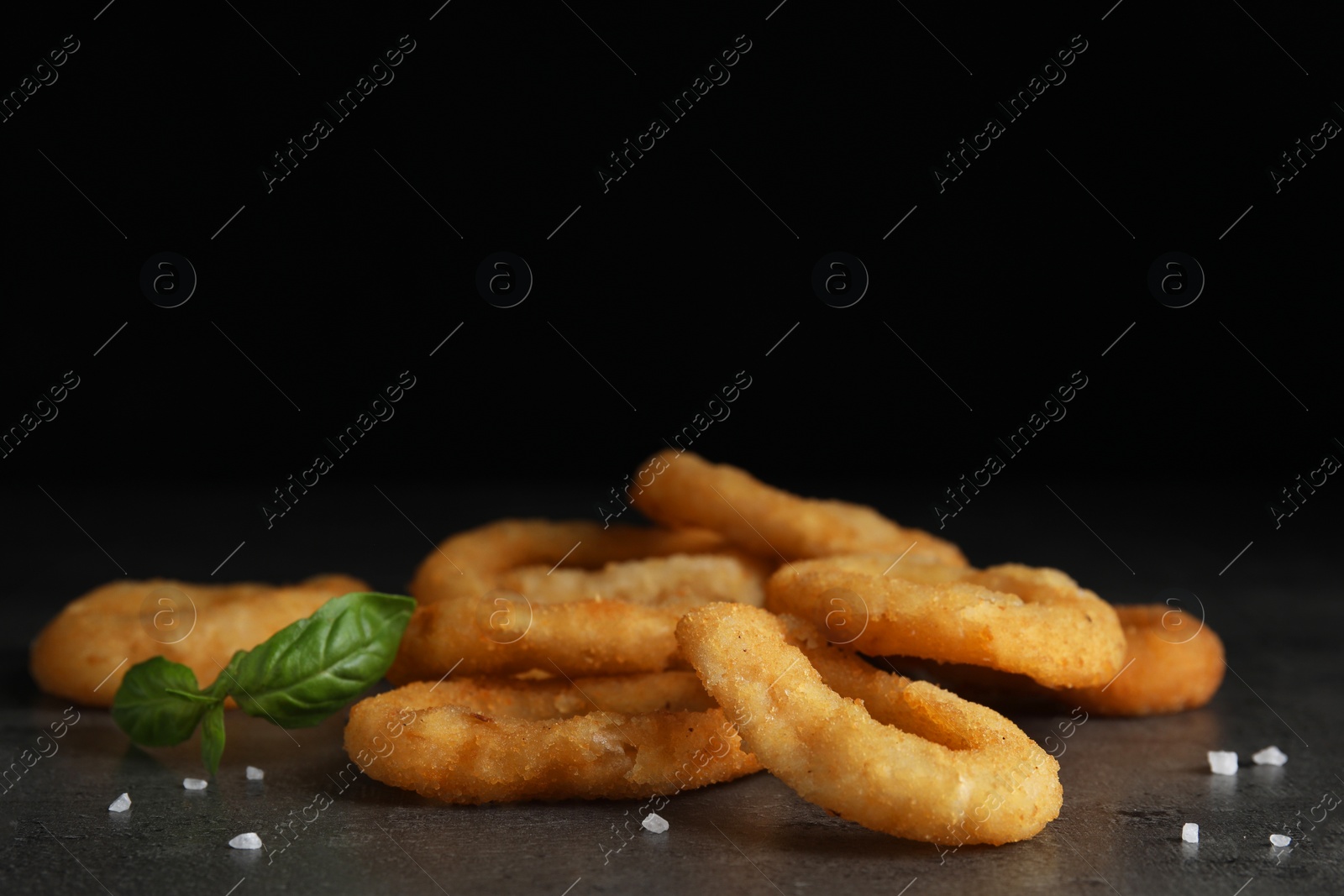 Photo of Fried onion rings and basil leaves on grey table