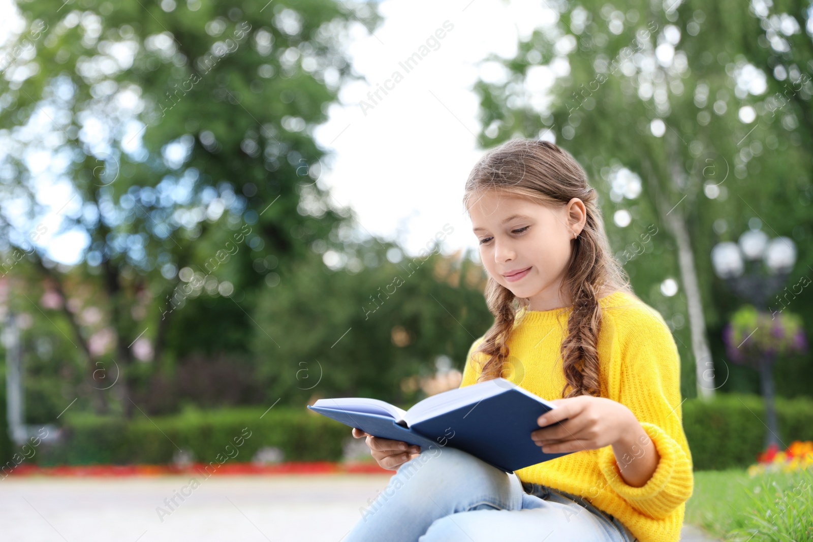 Photo of Cute little girl reading book in green park