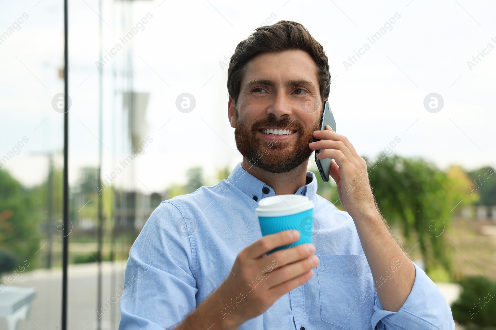 Photo of Handsome man with cup of coffee talking on phone outdoors