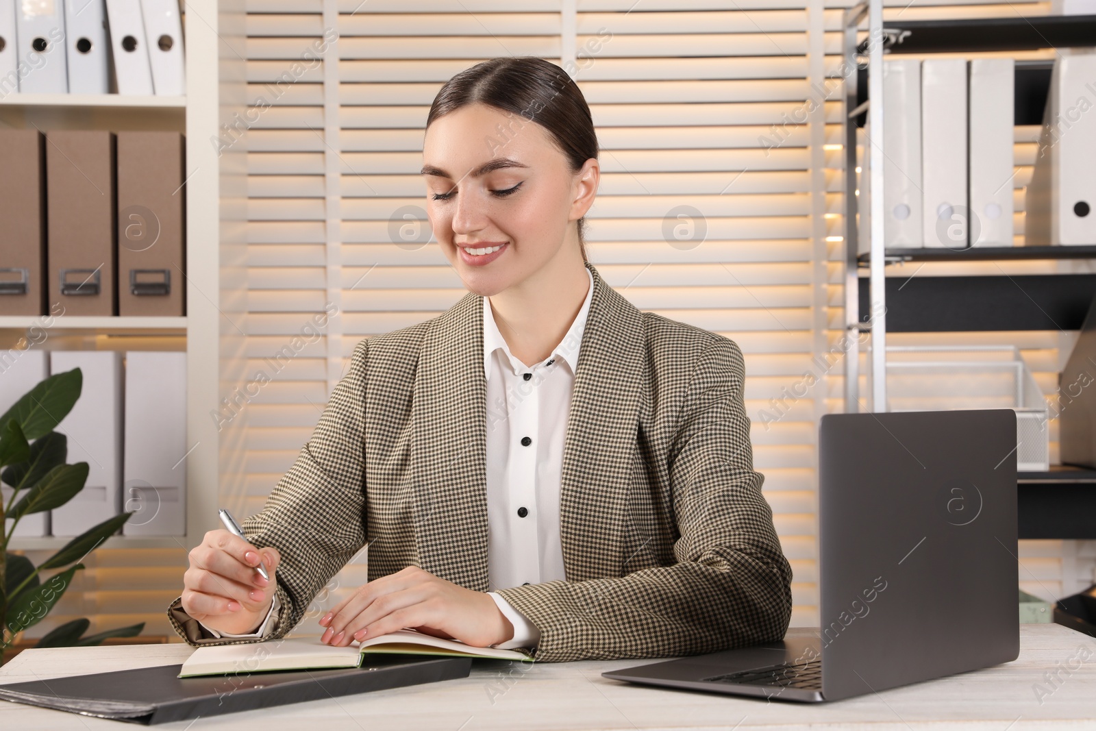 Photo of Happy woman taking notes at light wooden table in office