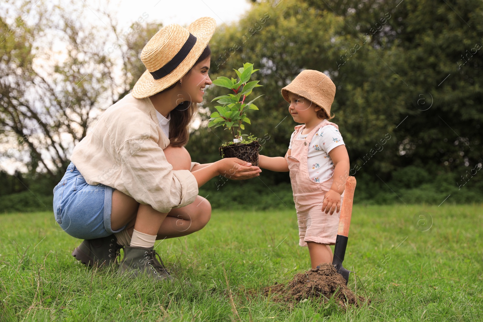 Photo of Mother and her baby daughter planting tree together in garden