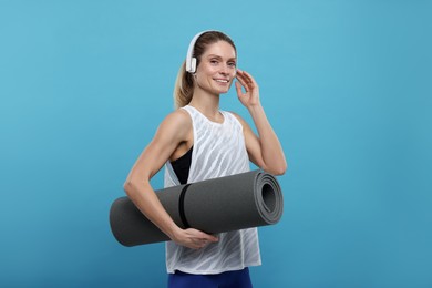 Photo of Sportswoman with headphones and fitness mat on light blue background, space for text