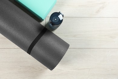 Photo of Exercise mat, yoga block and bottle of water on light wooden floor, flat lay. Space for text