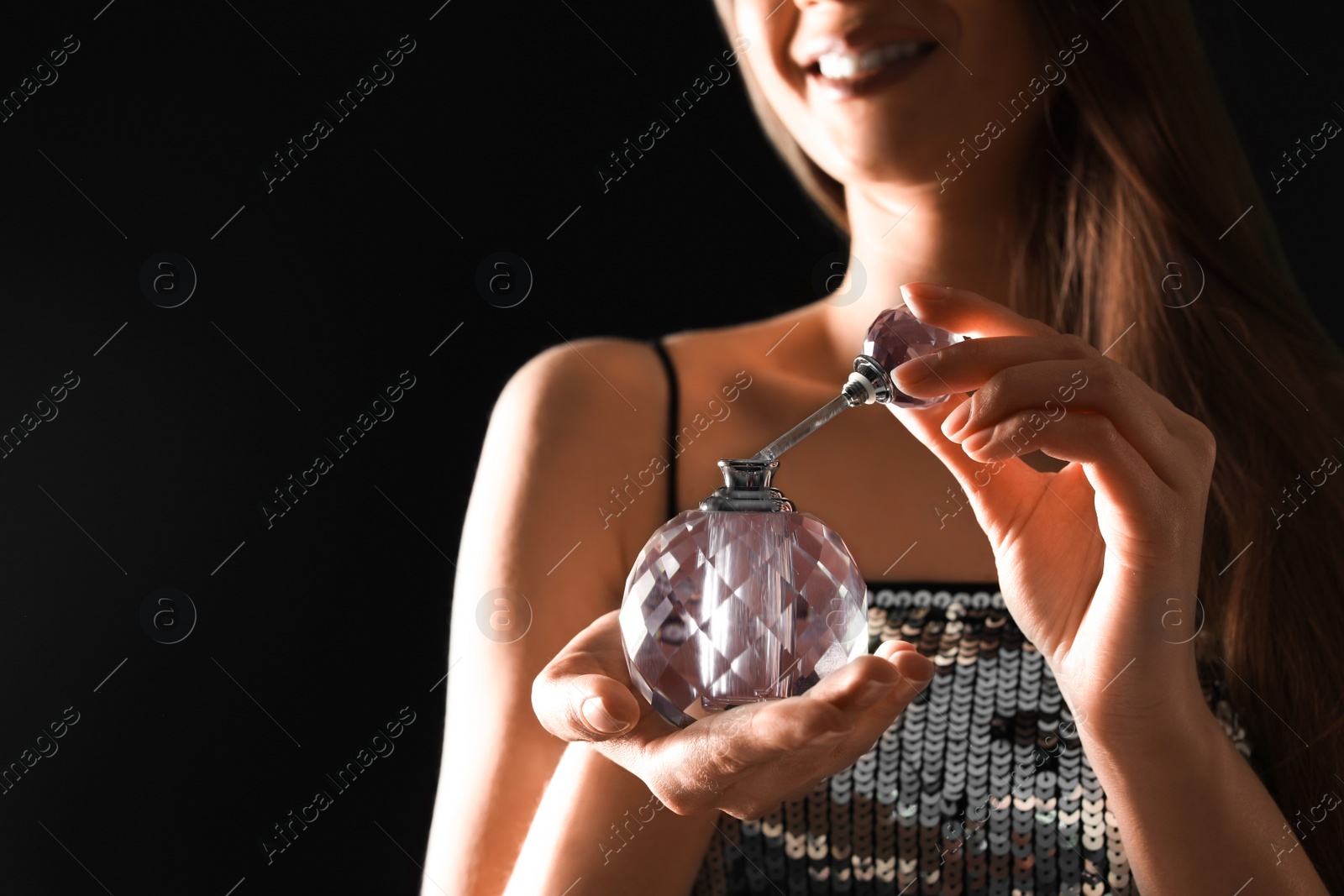 Photo of Young woman with bottle of perfume on black background, closeup. Space for text