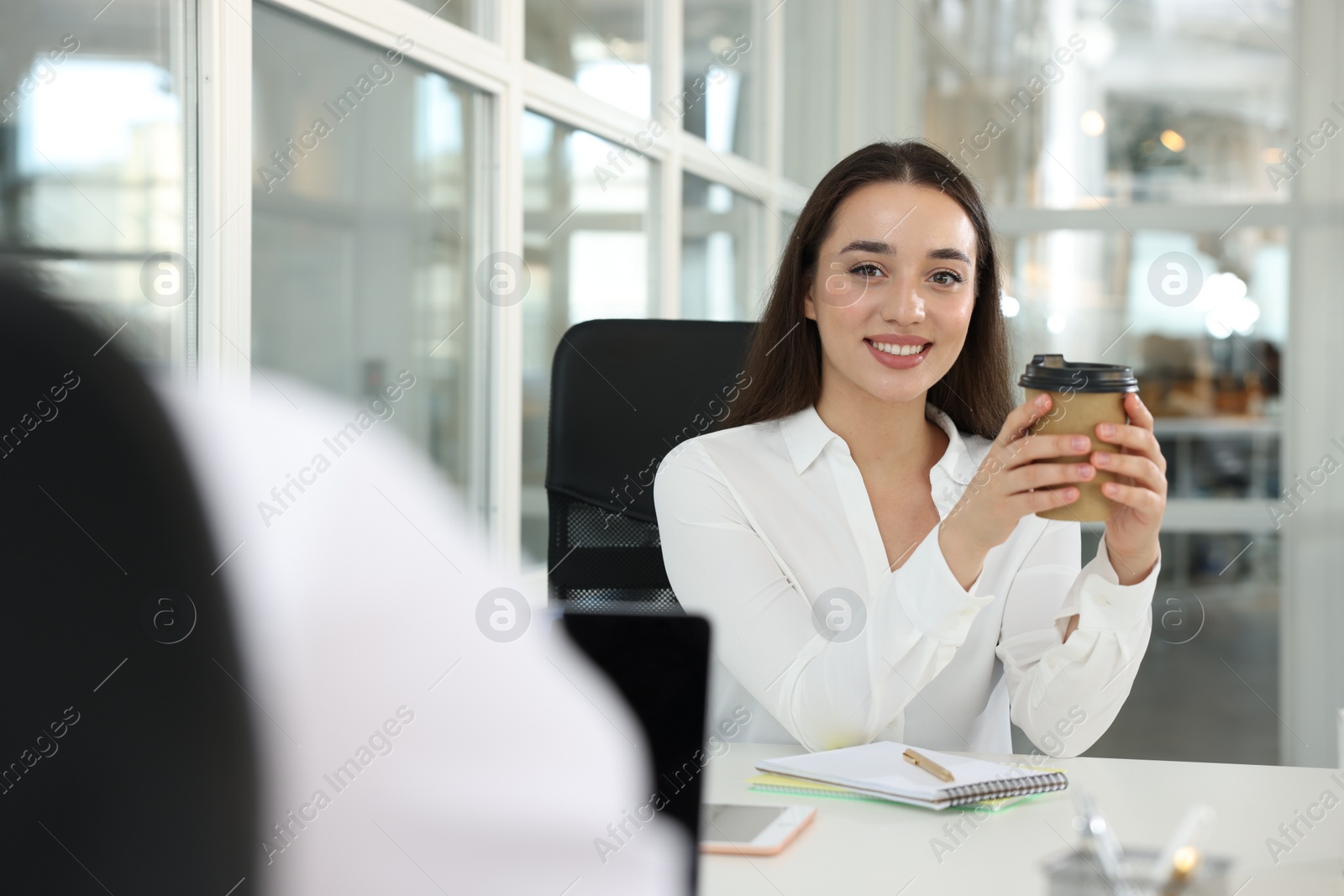 Photo of Happy woman with paper cup of coffee at desk in open plan office