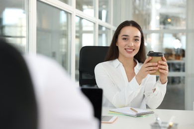 Photo of Happy woman with paper cup of coffee at desk in open plan office