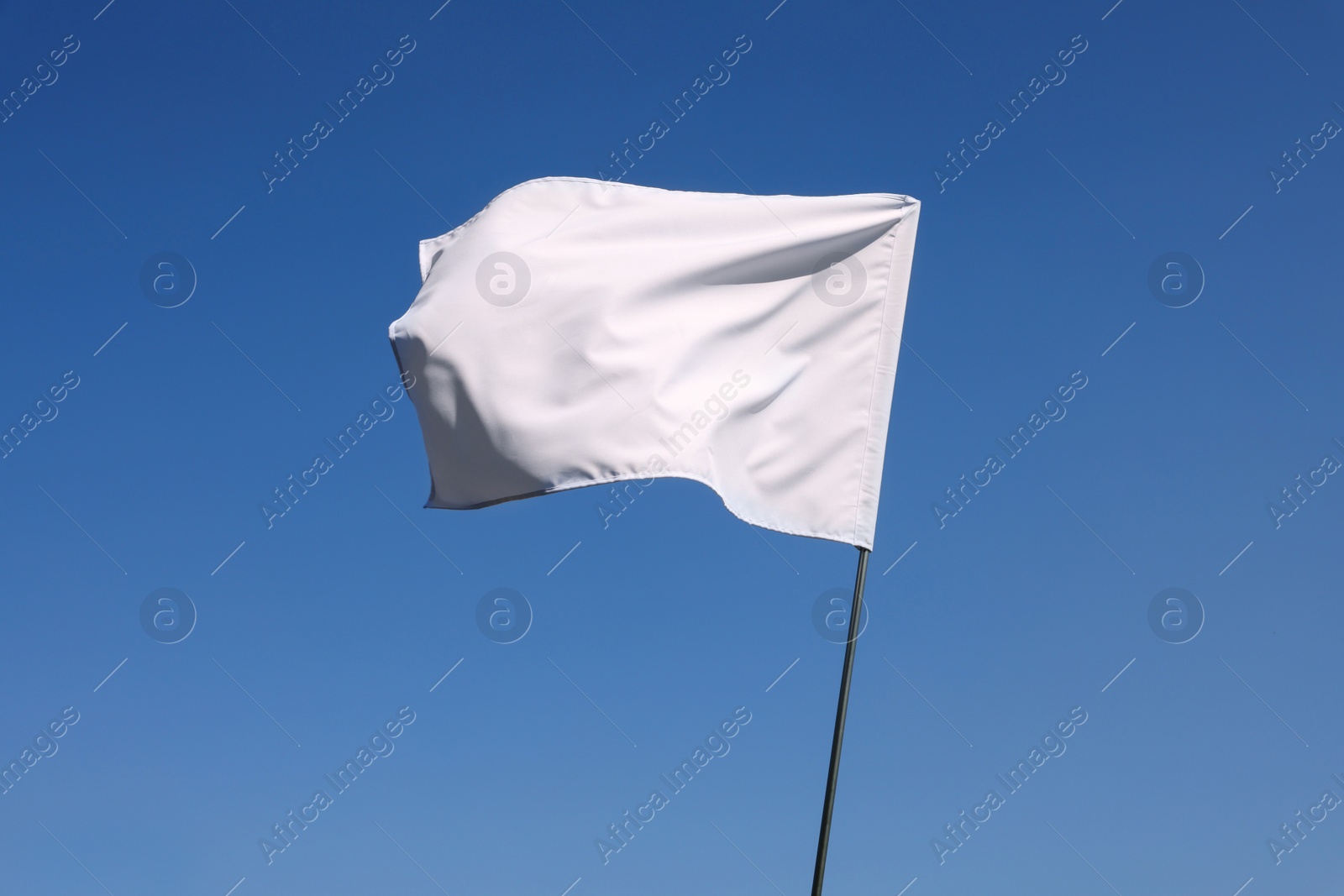 Photo of White flag fluttering against blue sky on sunny day