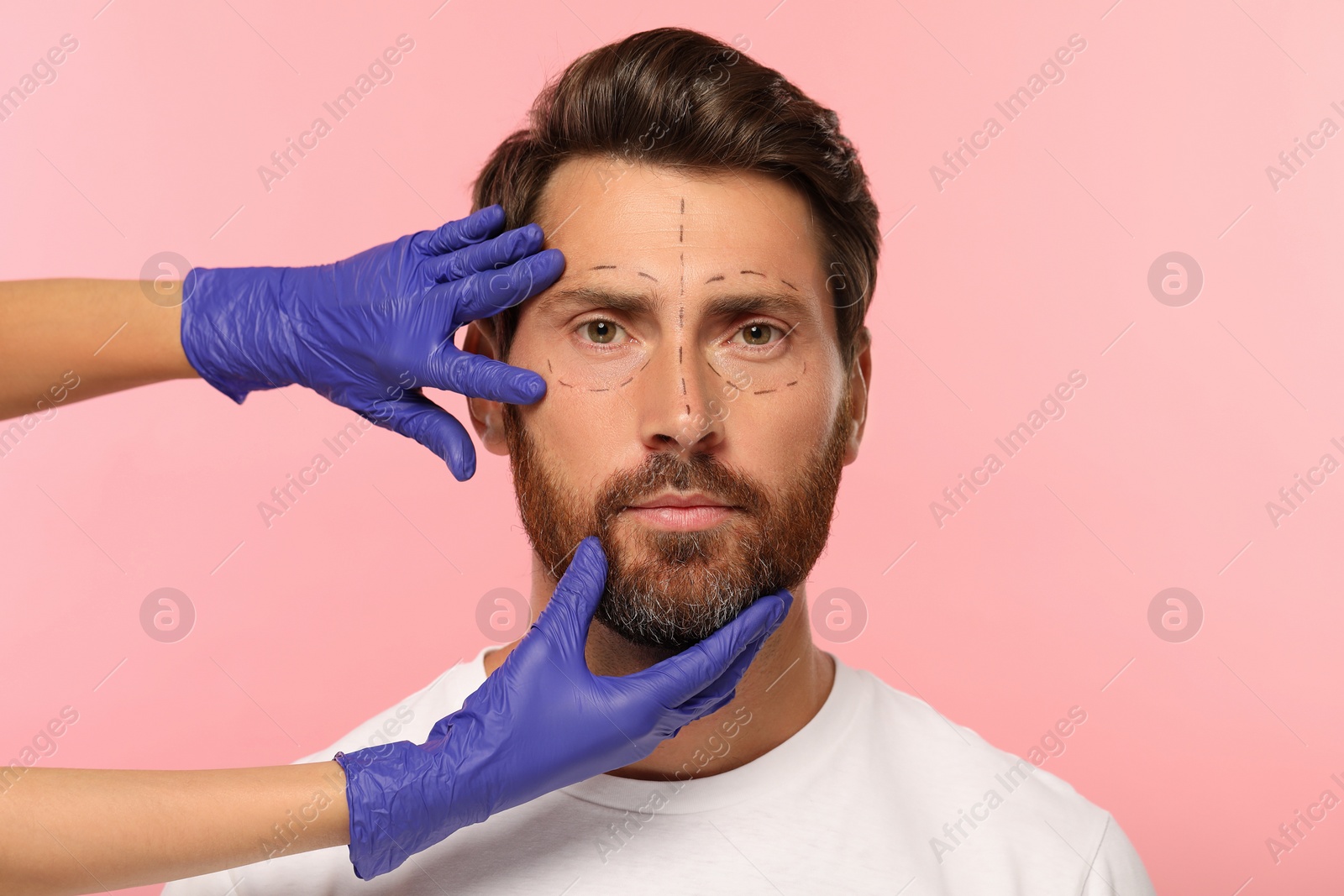 Photo of Doctor checking patient's face before cosmetic surgery operation on pink background