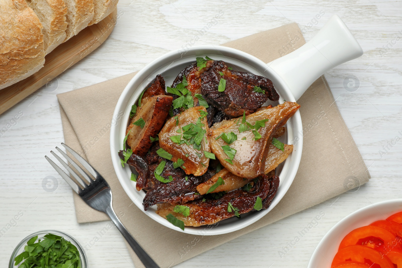 Photo of Tasty fried cracklings with parsley on white wooden table, flat lay. Cooked pork lard