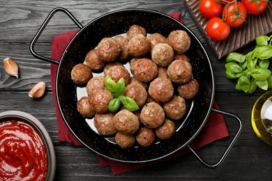 Photo of Tasty cooked meatballs with basil on black wooden table, flat lay