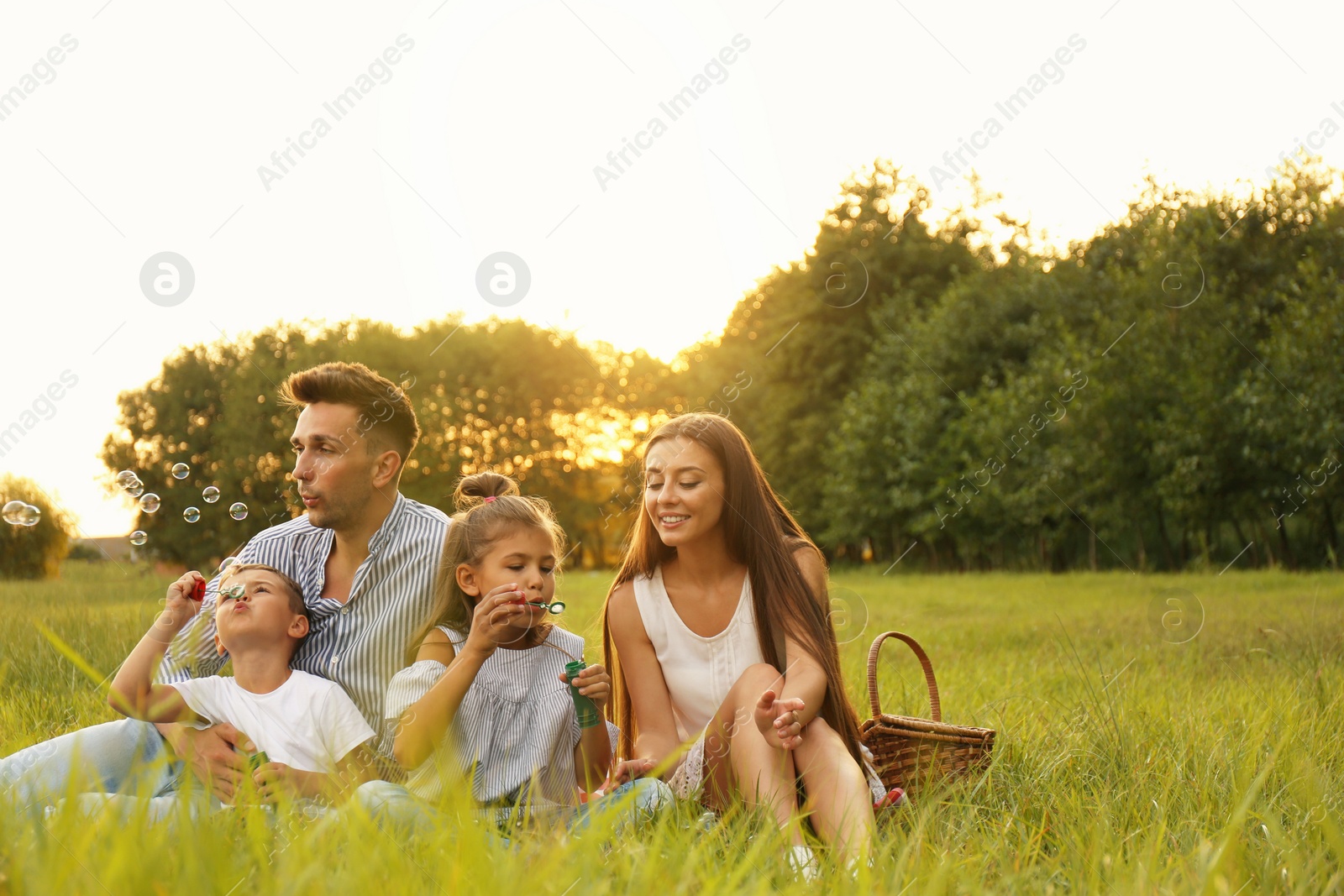 Photo of Happy family blowing soap bubbles in park at sunset. Summer picnic