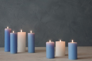 Burning candles on table against color wall with space for text