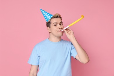 Young man with party hat and blower on pink background