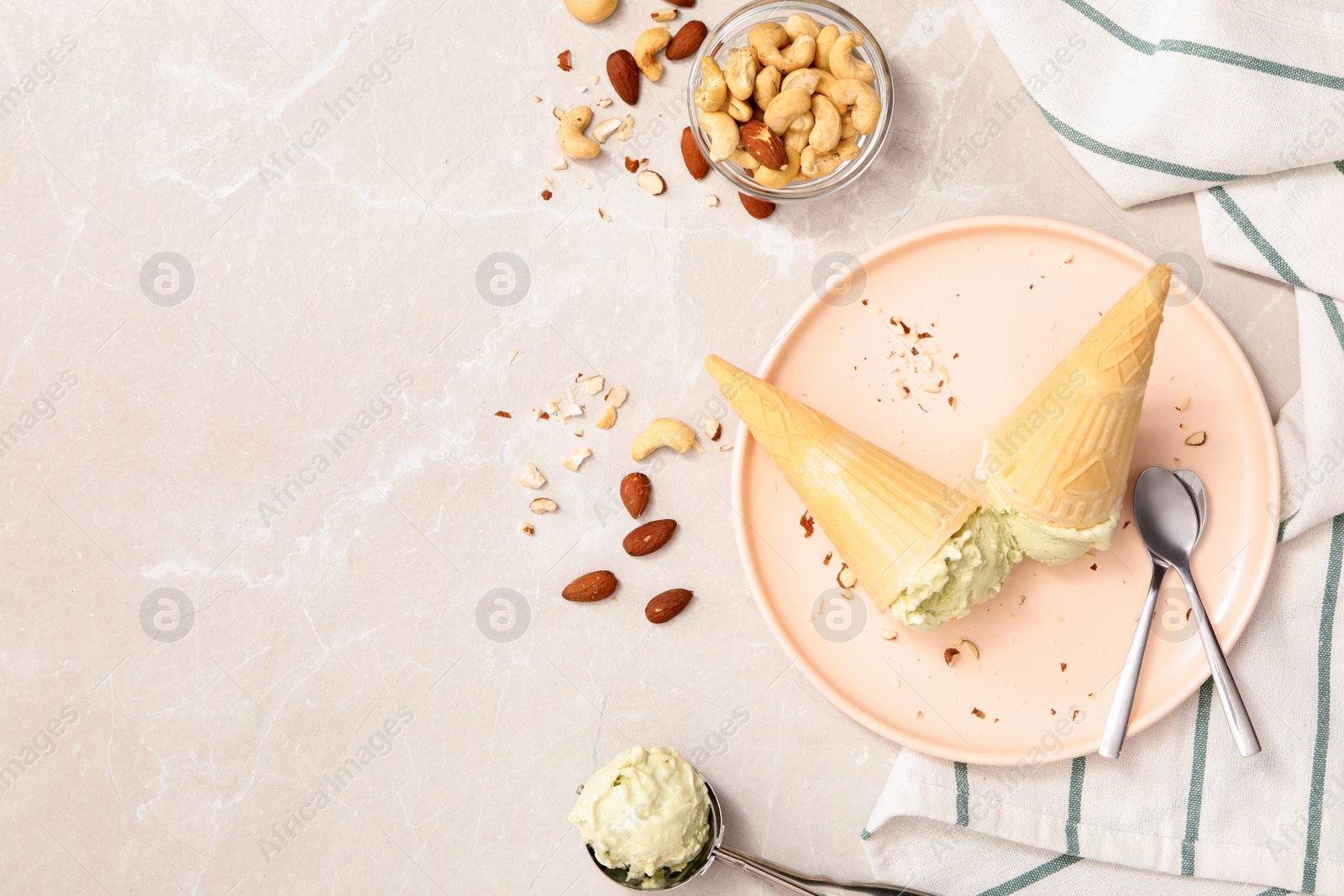 Photo of Delicious pistachio ice cream in wafer cones with chopped nuts served on light table, flat lay. Space for text