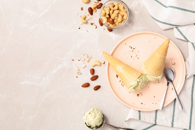 Photo of Delicious pistachio ice cream in wafer cones with chopped nuts served on light table, flat lay. Space for text