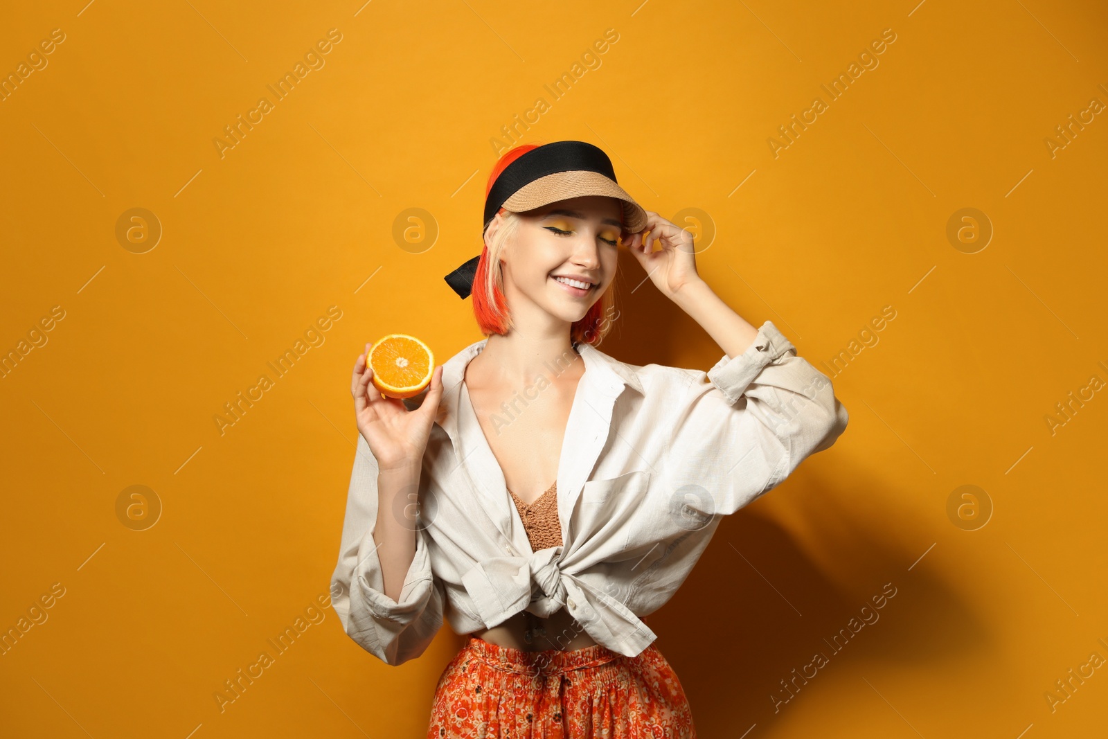 Photo of Beautiful young woman with bright dyed hair holding orange half on color background