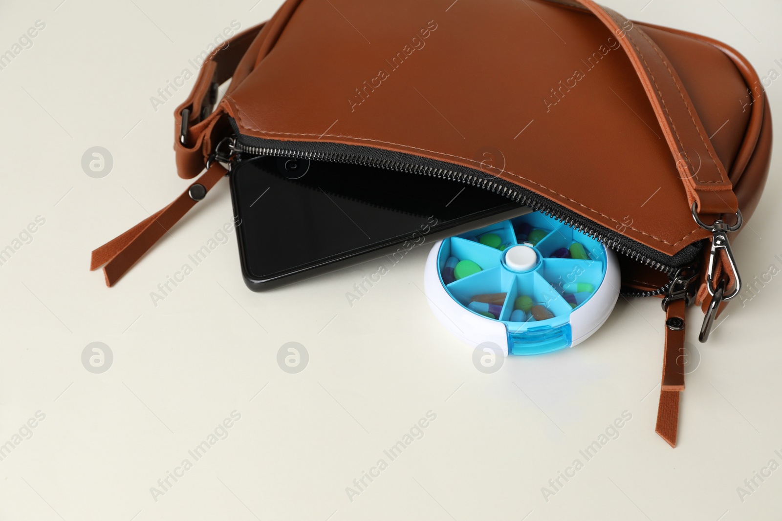 Photo of Pill box and smartphone sticking out of bag on white background, space for text