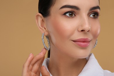 Beautiful young woman with elegant earrings on beige background, closeup