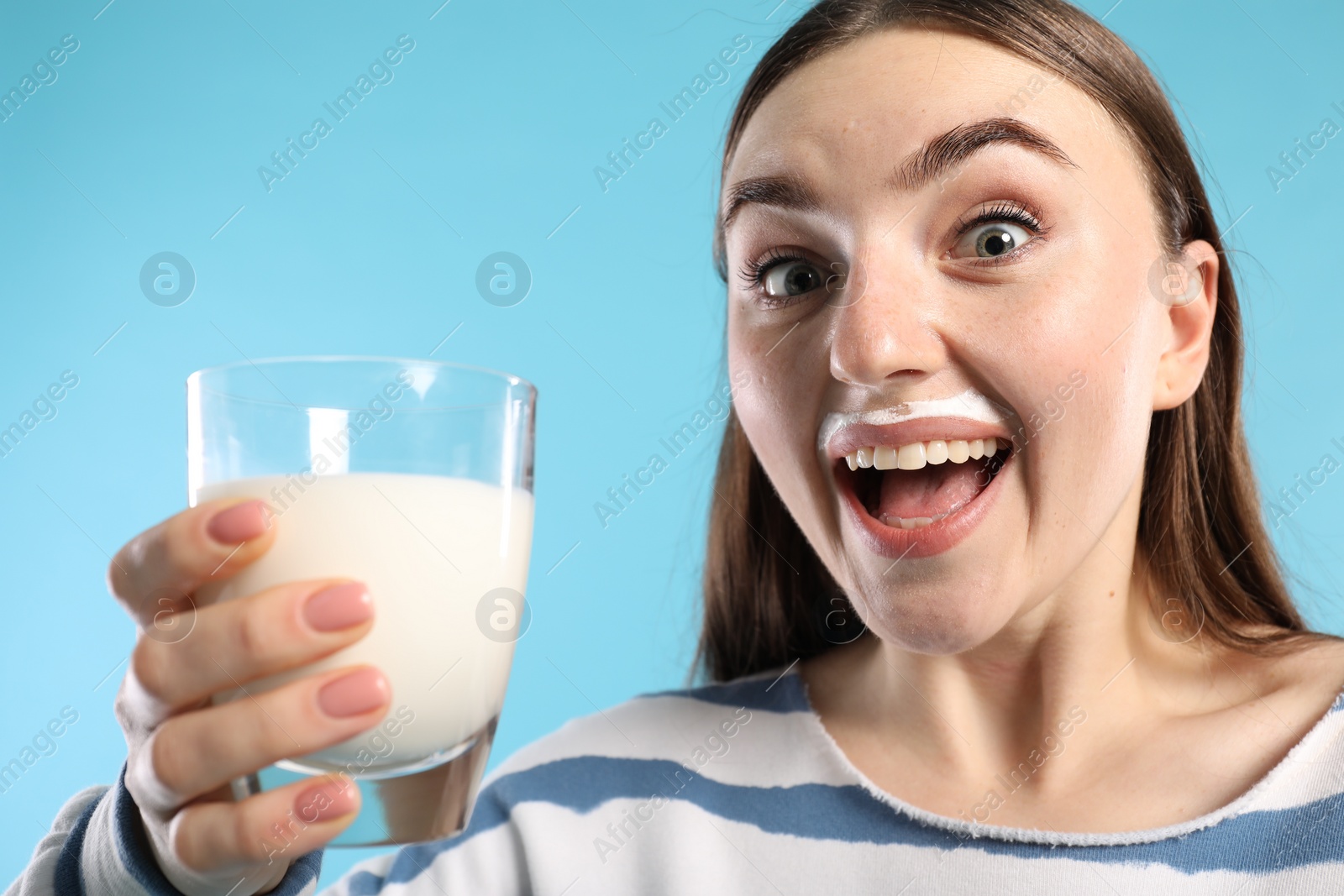 Photo of Emotional woman with milk mustache holding glass of tasty dairy drink on light blue background