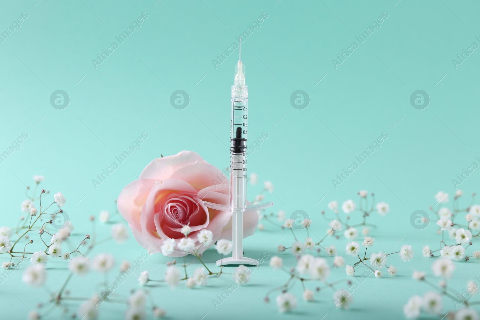 Photo of Cosmetology. Medical syringe, rose and gypsophila flowers on turquoise background