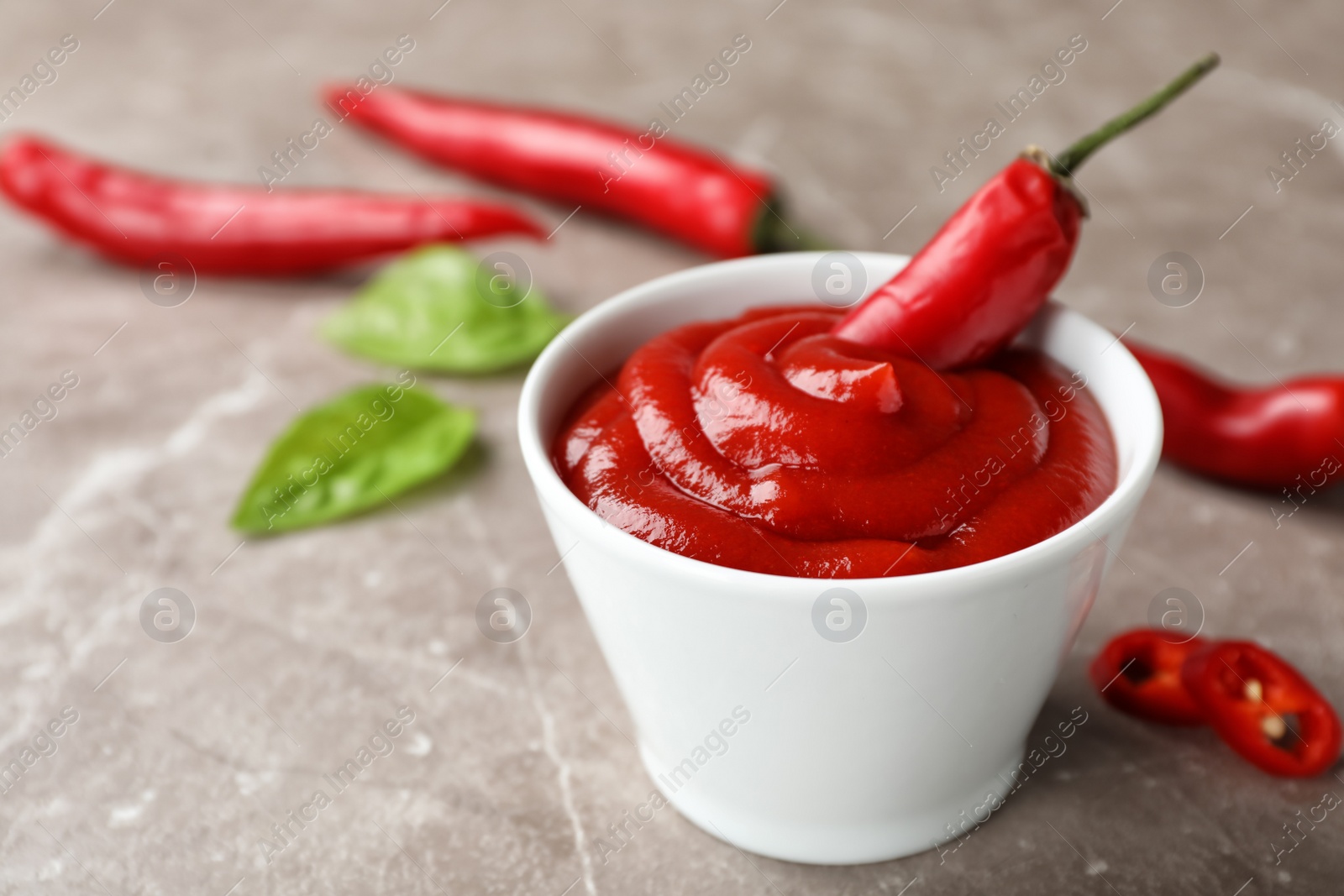 Photo of Bowl with spicy chili sauce and fresh pepper on gray table