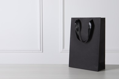 Black paper bag on white wooden table, space for text