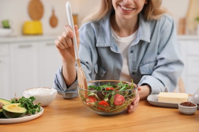 Photo of Woman with salad at wooden table in kitchen, closeup. Keto diet