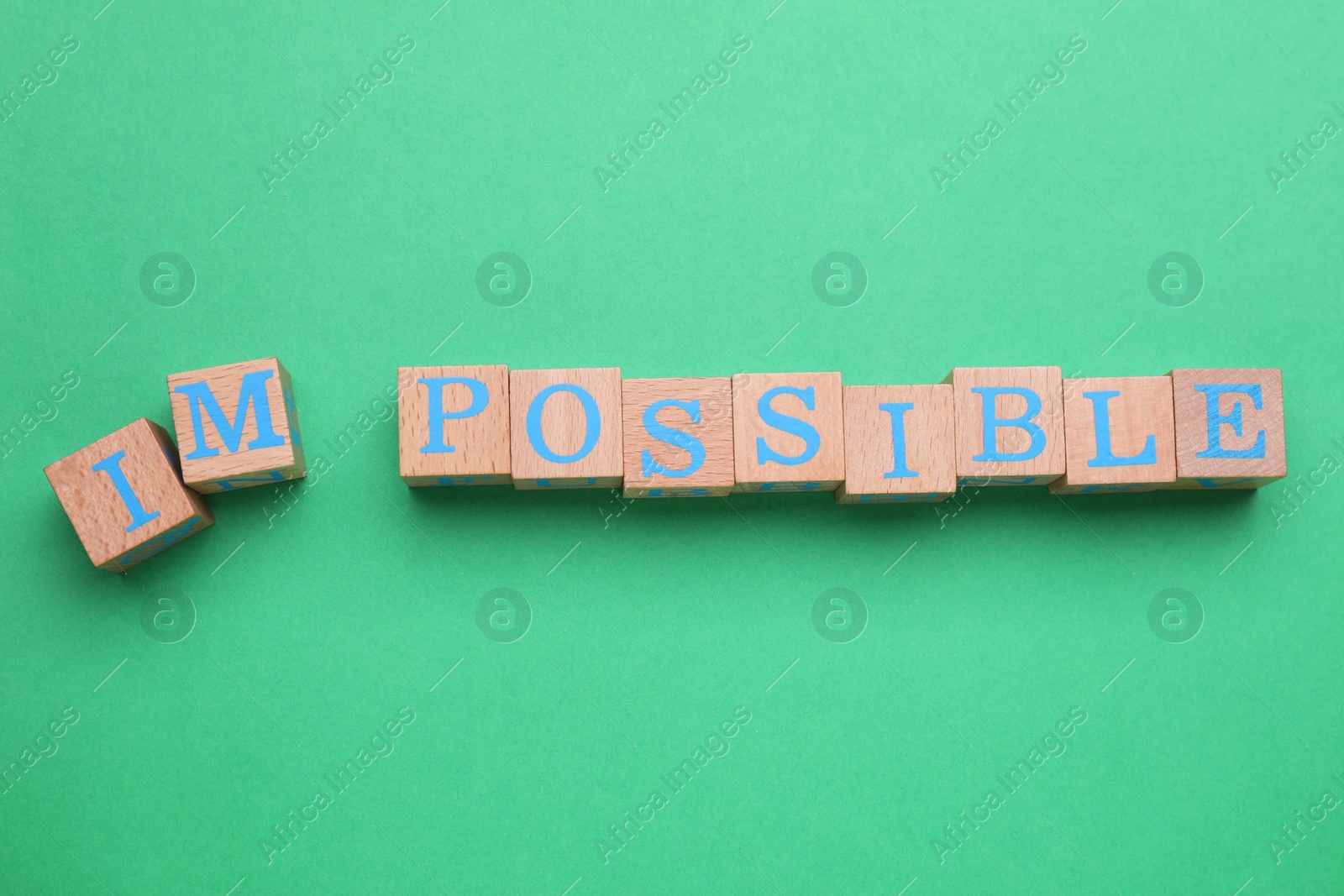 Photo of Motivation concept. Changing word from Impossible into Possible by removing wooden cubes with letters I and M on green background, top view