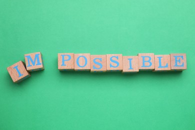Photo of Motivation concept. Changing word from Impossible into Possible by removing wooden cubes with letters I and M on green background, top view