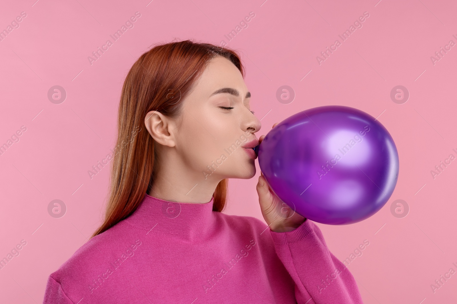 Photo of Woman inflating purple balloon on pink background