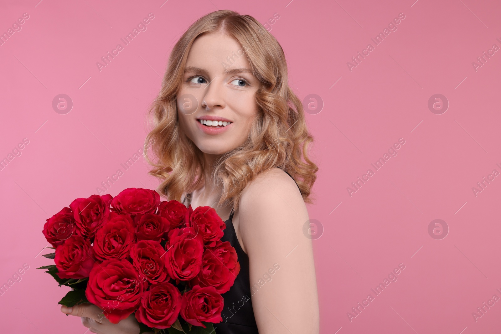 Photo of Beautiful woman with blonde hair holding bouquet of red roses on pink background. Space for text