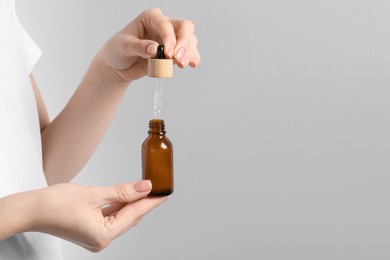 Woman dripping serum from pipette into bottle against light grey background, closeup. Space for text